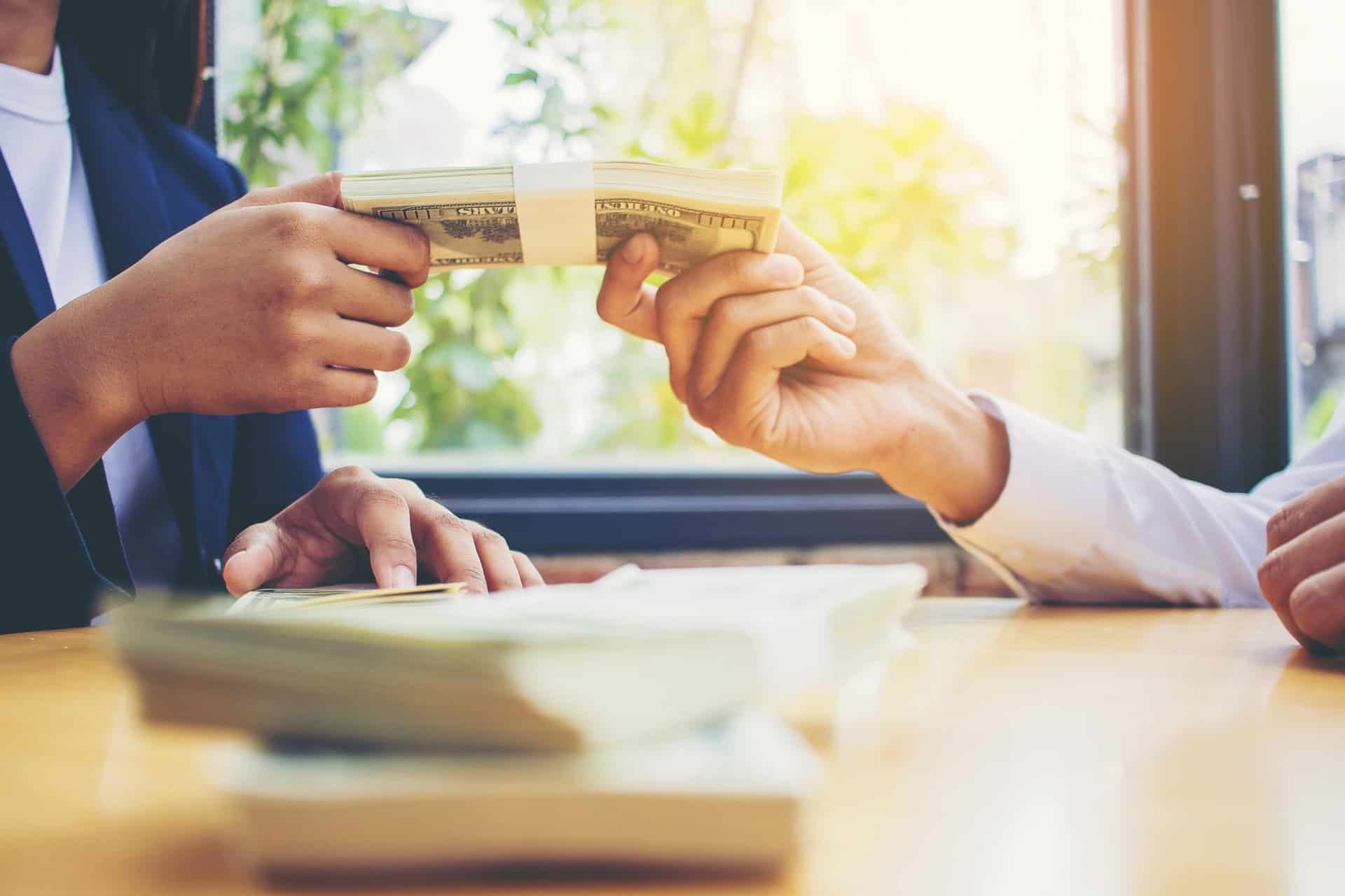 Business partners meeting and passing money for new business project on table.